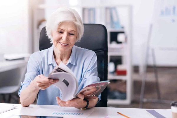 Smiling elderly businesswoman reading the magazine in the office
